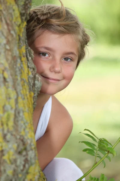 Ung flicka i vit klänning gömmer sig bakom ett träd — Stockfoto