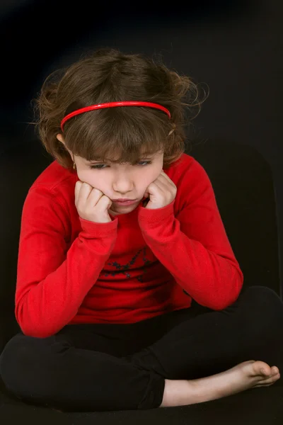 Маленькая девочка дуется лицом, опираясь на руки на черном фоне — стоковое фото