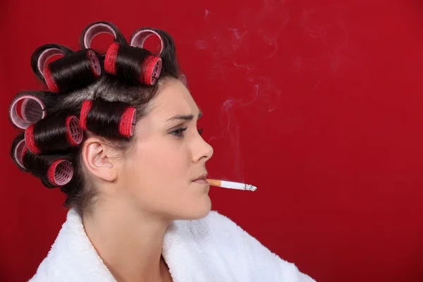 Žena s natáčky na vlasy proti kouření na červeném pozadí — Stock fotografie