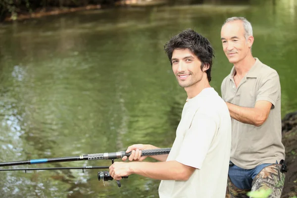 Un anciano y un joven pescando junto a un río — Foto de Stock