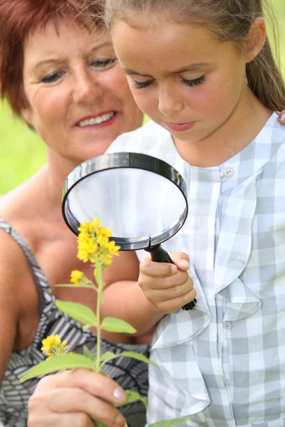 Girl and grandmother with magnifying glass — Stock Photo, Image