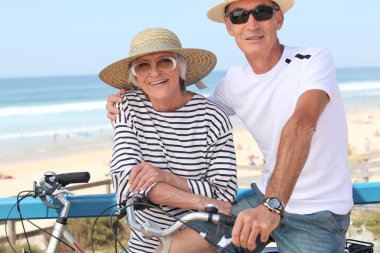 Senior couple riding bikes by the ocean clipart