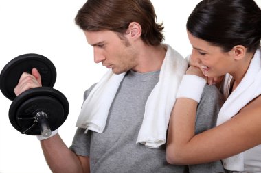 Young sporty man lifting weight encouraged by girlfriend clipart