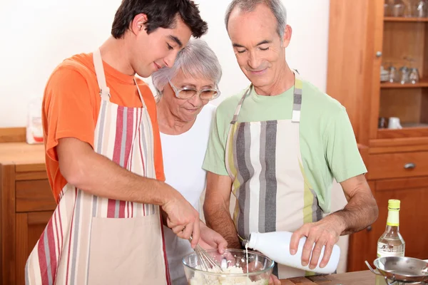 A 20 years old boy and 65 years old man and woman making cake together — Stock Photo, Image
