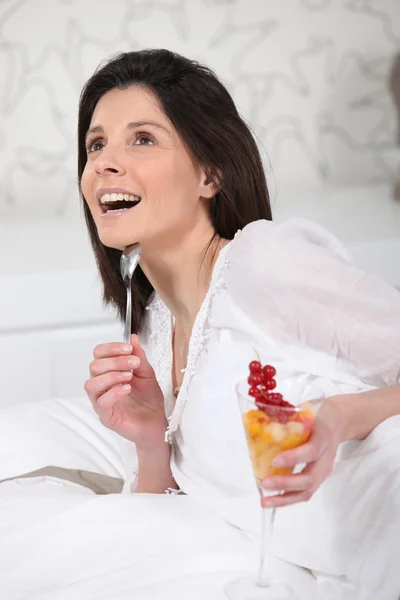 Frau liegt mit einem Glas Obstsalat auf ihrem Bett — Stockfoto