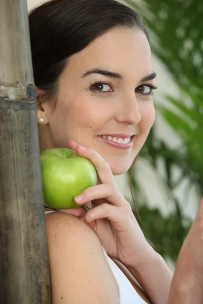 A brunette woman with an apple leaning against a bamboo stick — Stock Photo, Image