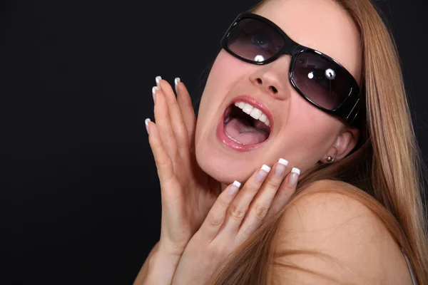 Mujer joven con gafas de sol gritando delante de un fondo negro — Foto de Stock