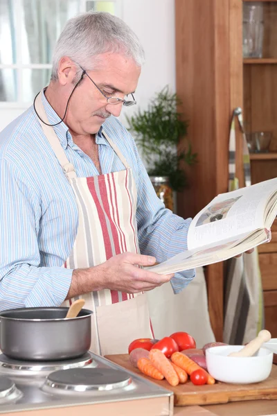 Senior citizen cooking with recipe book — Stock Photo, Image