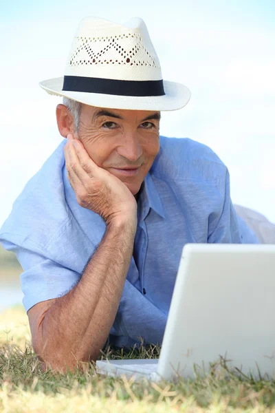 Senior man met zijn laptop liggen op het gras — Stockfoto