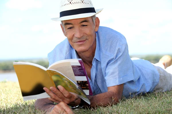 Пожилой джентльмен лежит на траве и читает туристический путеводитель — стоковое фото