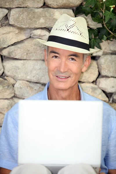 老人戴着一顶帽子和使用便携式计算机 — 图库照片