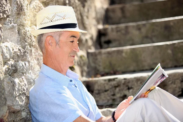 Senior man reading a magazine on some old stone steps — Stock Photo, Image