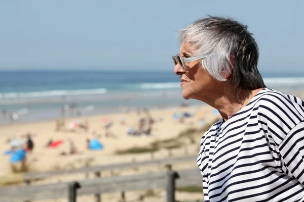 Старша жінка, яка дивиться на піщаний пляж в літній день — стокове фото