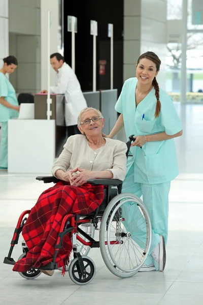 Enfermeira empurrando uma mulher mais velha em uma cadeira de rodas — Fotografia de Stock