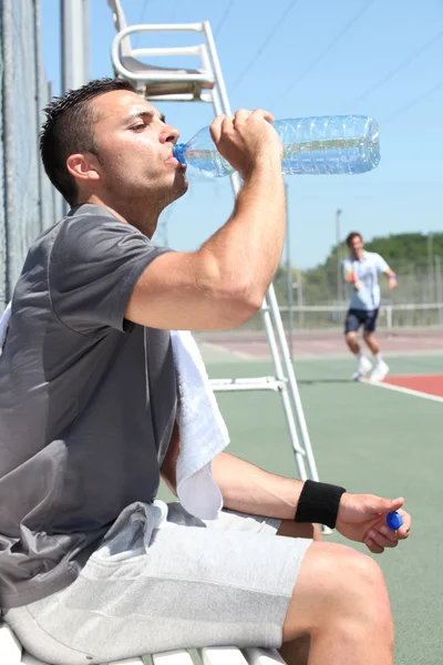 Uomo acqua potabile a bordo campo da tennis — Foto Stock
