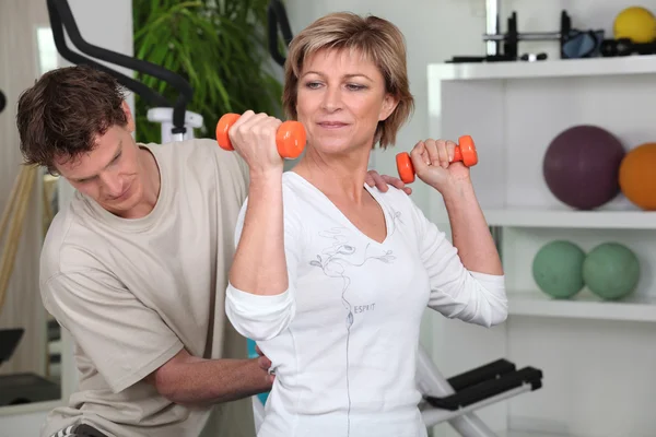 Mujer madura haciendo ejercicio con pesas y un entrenador personal — Foto de Stock