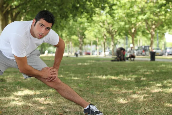 Młody człowiek robi ćwiczenia rozciągające w parku — Zdjęcie stockowe