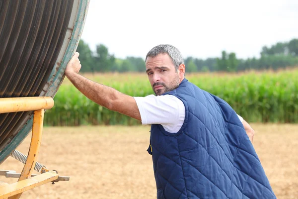Farmář v poli s naviják hadice — Stock fotografie