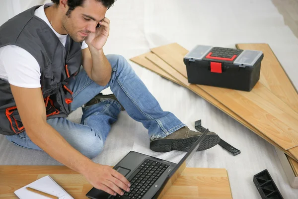 Człowiek z laptopa, układanie podłóg laminowanych — Zdjęcie stockowe