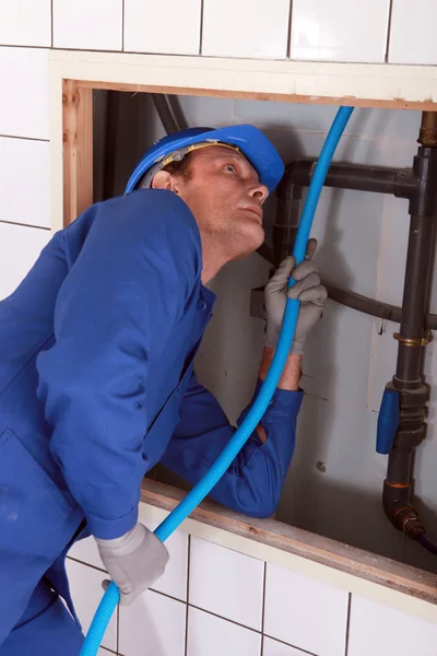 Plombier alimentant tuyau bleu derrière un mur carrelé — Photo