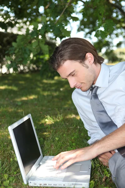 Smart male executive using a laptop with a blank screen in the park — Stock Photo, Image