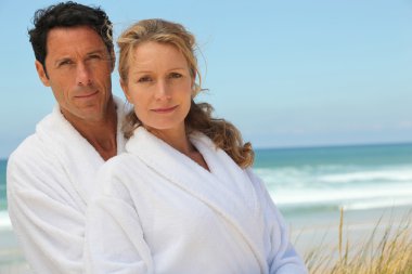 Husband and wife on the beach in bath robes clipart