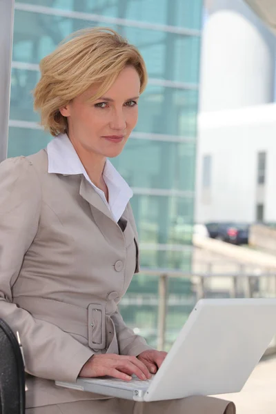Businesswoman on laptop outside airport — Stock Photo, Image