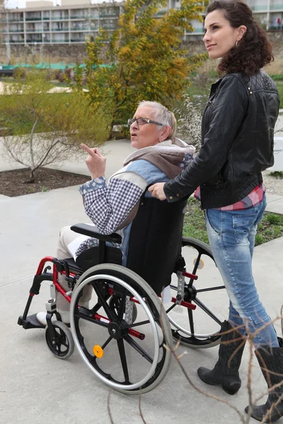 Молода жінка штовхає старшу жінку в інвалідному візку — стокове фото