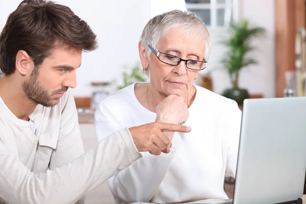 Hombre joven mostrando a una mujer mayor cómo utilizar un ordenador portátil —  Fotos de Stock