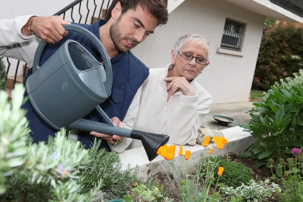 Young man watering plants with older woman — Stock Photo, Image