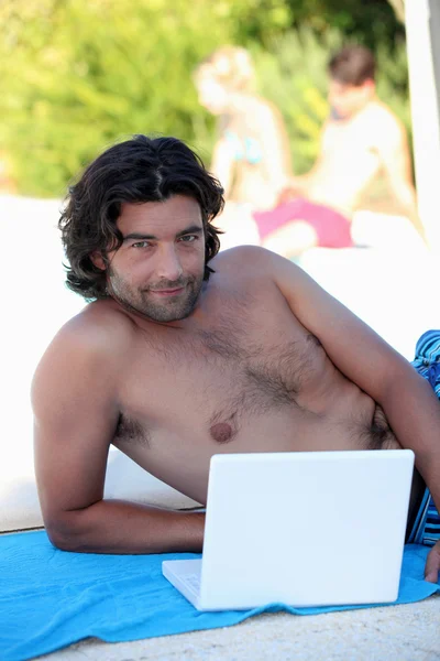 Мужчина лежит на пляжном полотенце с ноутбуком — стоковое фото