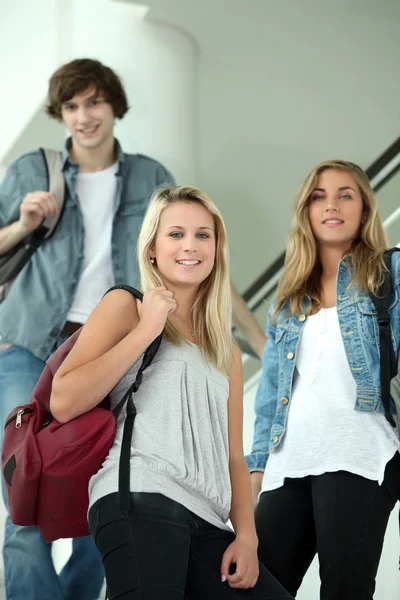 Trzech studentów uśmiechający się chodzenie w dół schodów wewnętrznych — Zdjęcie stockowe