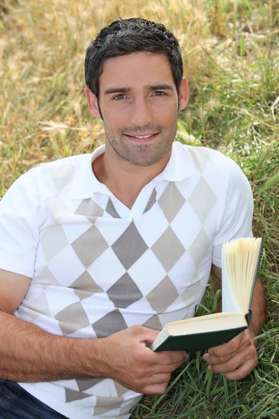 Чоловік лежить у полі з книгою в руці — стокове фото