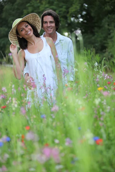 Feliz pareja joven en la hierba alta en medio de flores silvestres — Foto de Stock