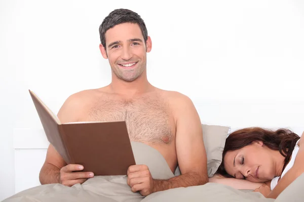 Čtení v posteli, jako jeho partner spí muž — Stock fotografie