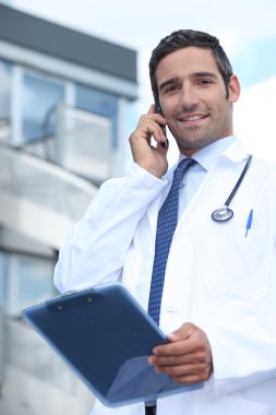 Doctor using his mobile phone outside a hospital building clipart