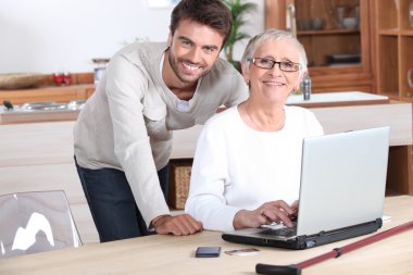 Young man helping senior woman with a laptop compute clipart