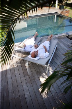 Elderly couple on sunloungers by a pool clipart