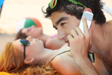 Young man phoning at the beach with his friends clipart