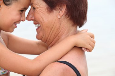 Grandmother nose to nose with her granddaughter on the beach clipart