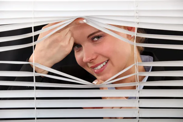 Vrouw op zoek via de blinds — Stockfoto