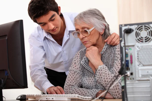 Junger Mann zeigt älterer Dame, wie man Computer benutzt — Stockfoto