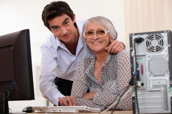 Jonge man helpt een oudere dame die een computer gebruiken — Stockfoto