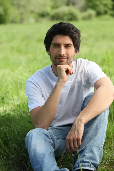 Portret przystojny młody mężczyzna siedzi na trawie — Zdjęcie stockowe