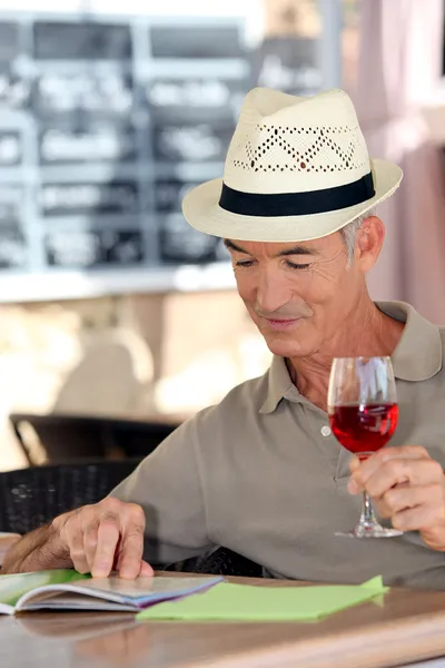 Uomo anziano che beve un bicchiere di rosa in un caffè — Foto Stock