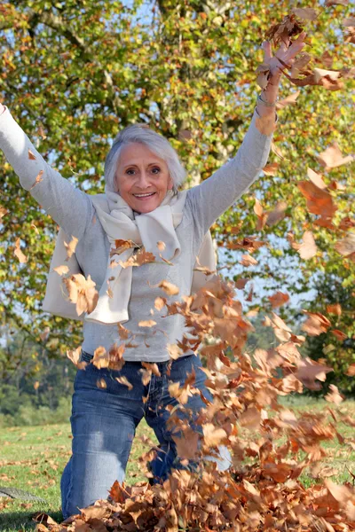 Grandmother playing with a heap of dead leaves — Stock Photo, Image