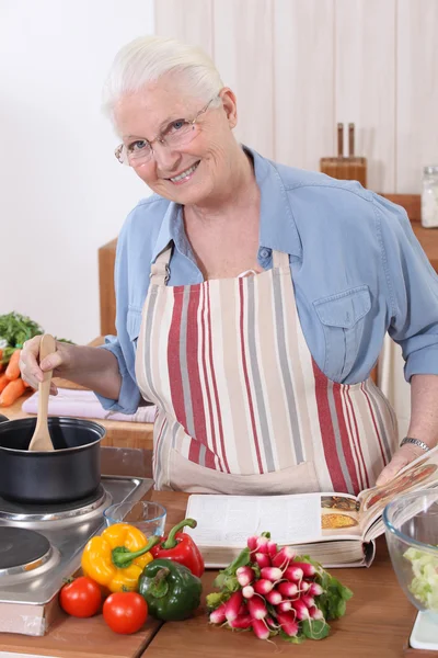 Ηλικιωμένη γυναίκα μαγείρεμα με τη βοήθεια μιας συνταγής — Φωτογραφία Αρχείου