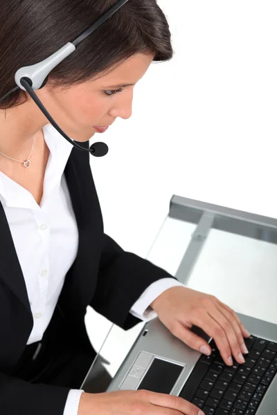 Ung kvinna som bär ett headset att skriva på ett tangentbord — Stockfoto