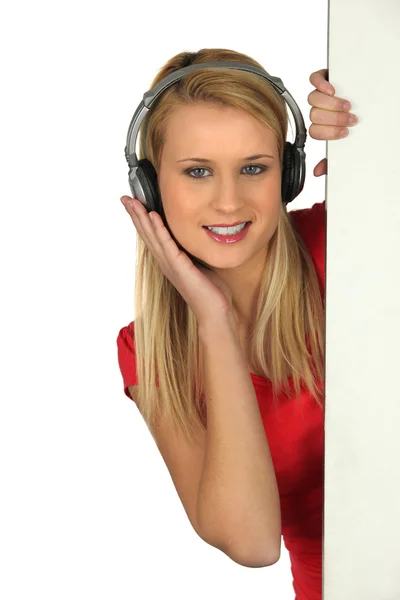 Girl with earphones hidden behind a panel — Stock Photo, Image