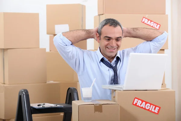 Man omringd door kartonnen dozen met behulp van zijn laptop — Stockfoto